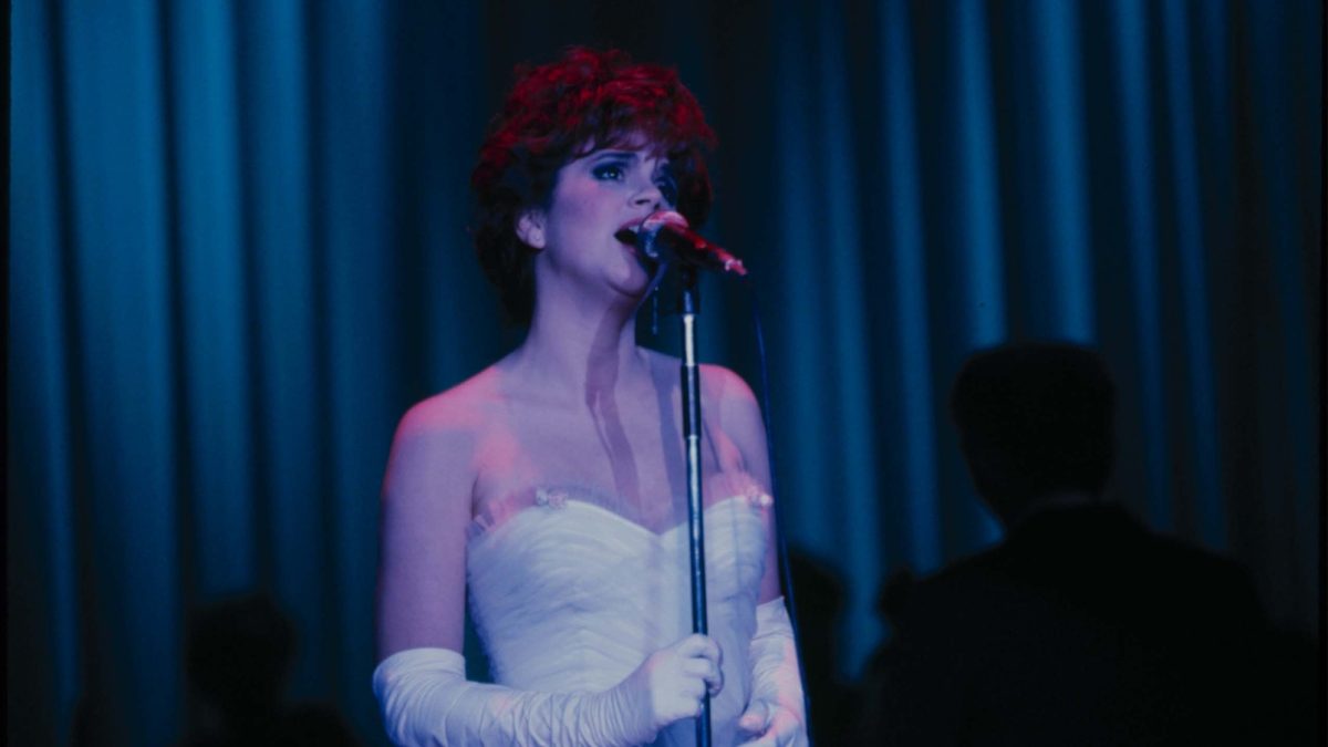Linda Ronstadt in a white strapless dress and matching gloves, singing in front of a mic