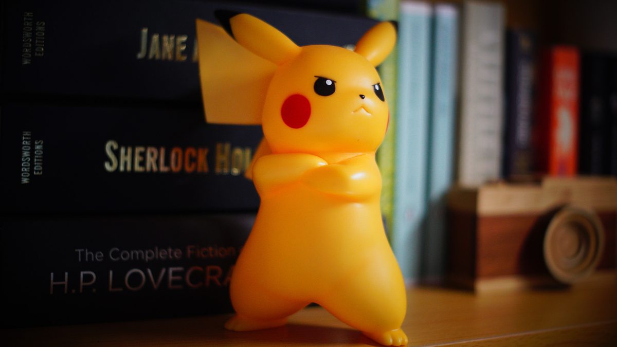 An angry Pikachu toy on the wooden shelf with many books in the background