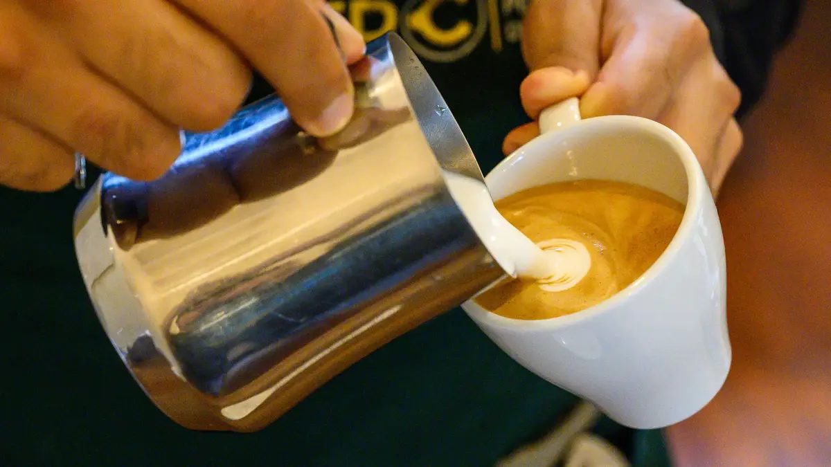 Professional barista pouring latte foame over coffee, espresso and creating a perfect cappuccino