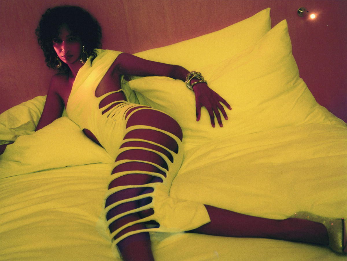 Nancy Uddin reclines on a bed in a revealing white dress