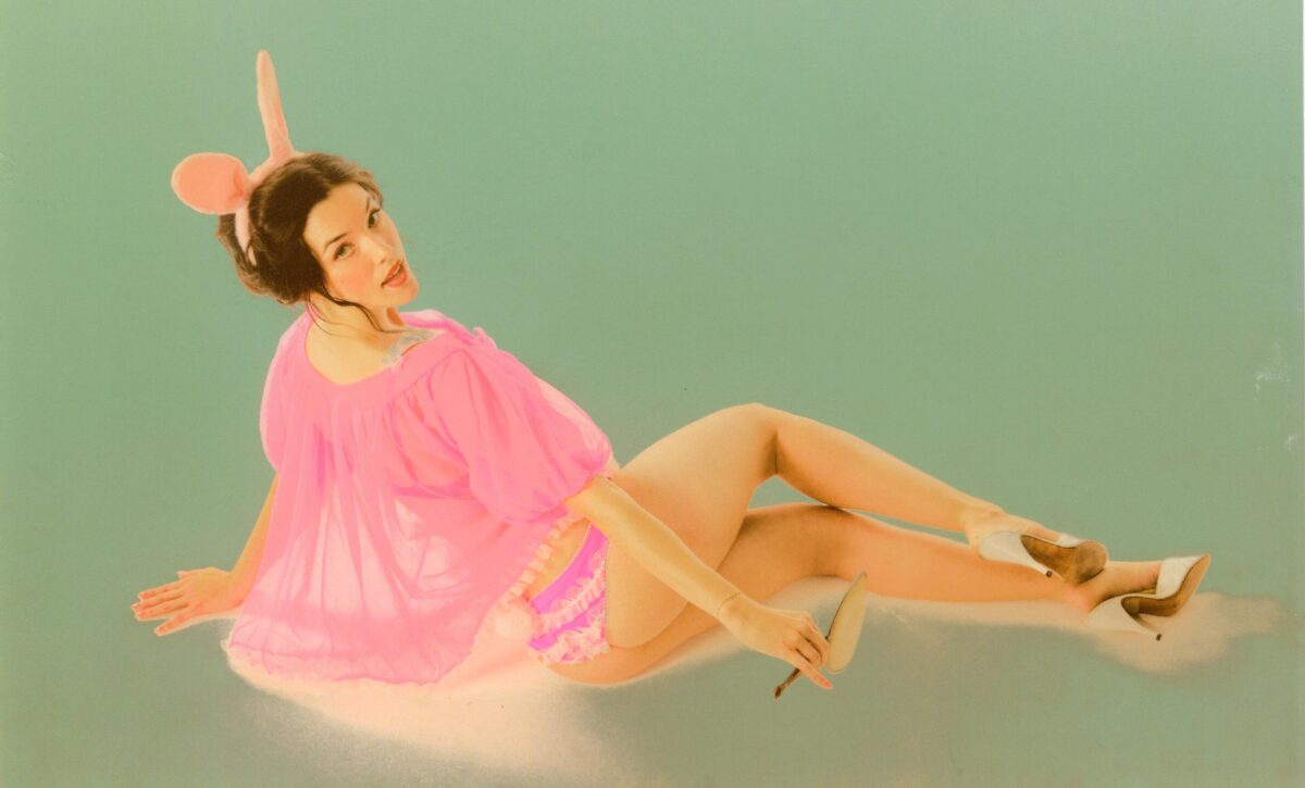 Lauren Summer in a pink nightie with pink bunny years, reclining against a green background.
